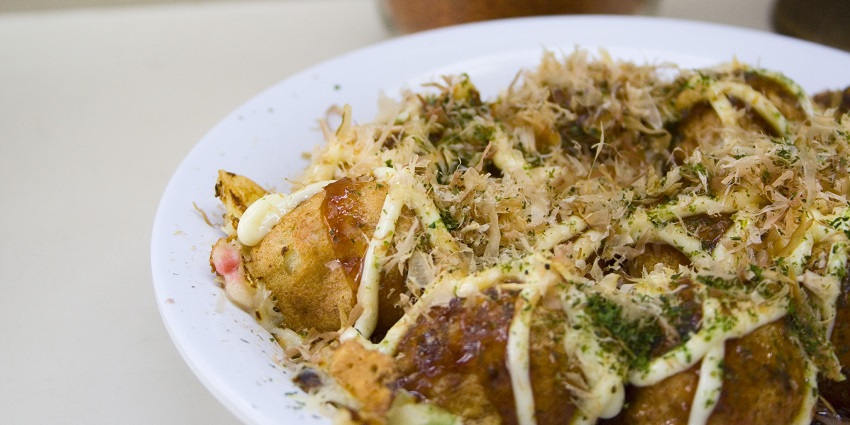 Takoyaki is served with delicious sauce toppings at a restaurant, a street food in Toronto.