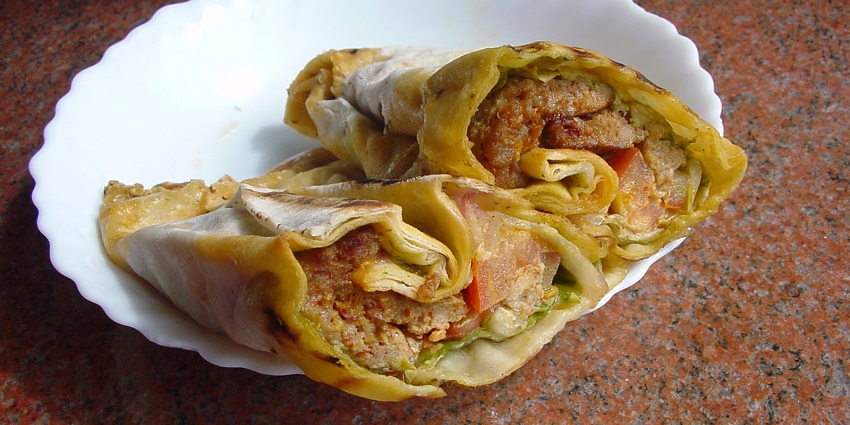Lamb wrap divided into two pieces on a small white plate over a brown marble slab.