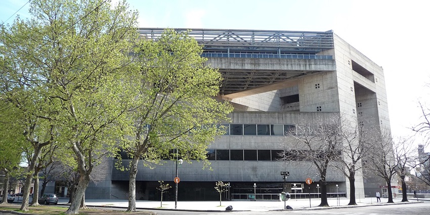A frontal view of a tall building with glass windows and a sizable compound in front