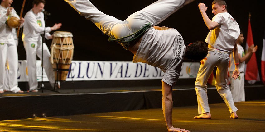 Capoeira performers displaying acrobatic moves and rhythmic dance during a street show.
