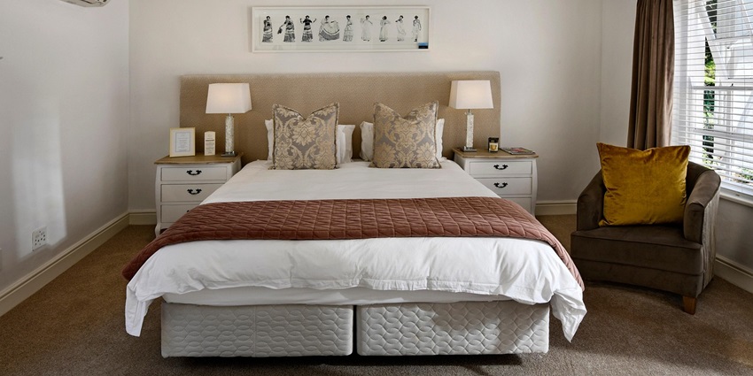 An image showing a hotel bedroom featuring a bed, lighting, and arranged furnishings.