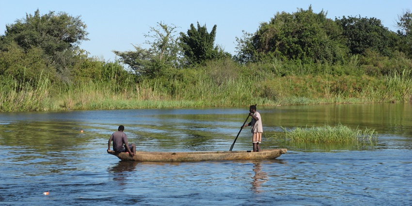 Two local fishermen paddling a canoe across the wide Zambezi River under bright sunlight.