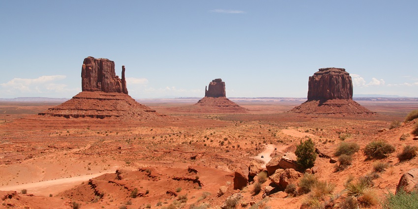 Red sandstone towers rise from a flat desert floor with a dirt road stretching through the valley.