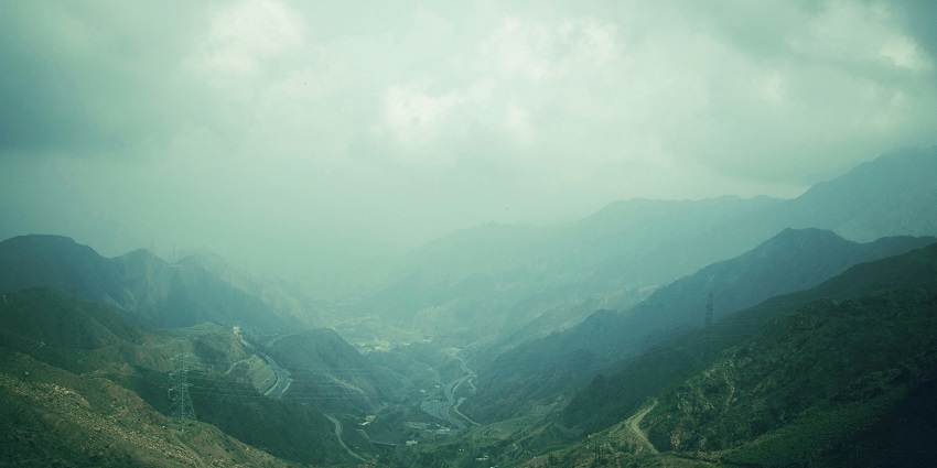 An empty road runs through the town of Abha, and a lush green hill runs along the way.