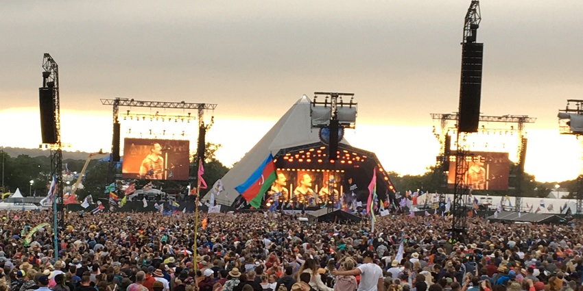 Pyramid stage in Glastonbury festival with an ongoing concert and crowd holding flags