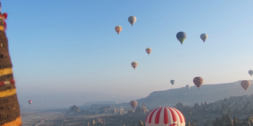 Hot air balloons are in the air as the city sprawls below and the blue sky stretches