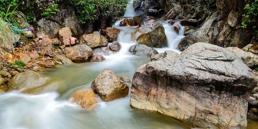 Two parallel streams of water cascade side by side through rocks into a clear pool.