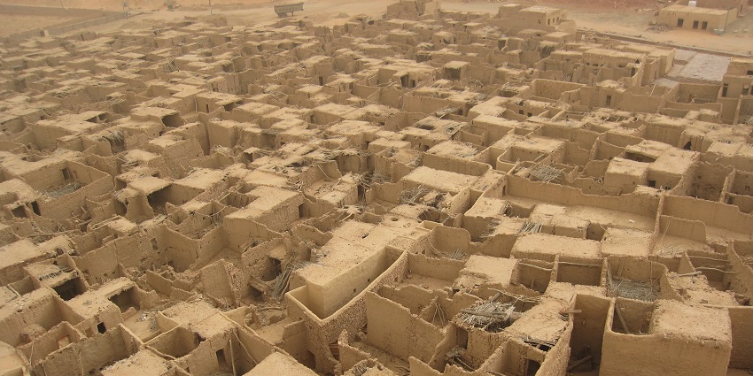 Aerial view of a desert village, AlUla, with closely packed mud-brick houses in sandy terrain.