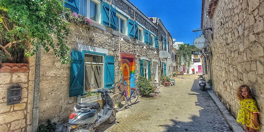 An image showing Alaçatı sokakları with narrow streets, shops, and traditional stone houses.