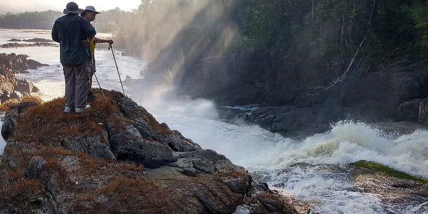 Amatuk Falls flowing in the background with two people standing near the water’s edge