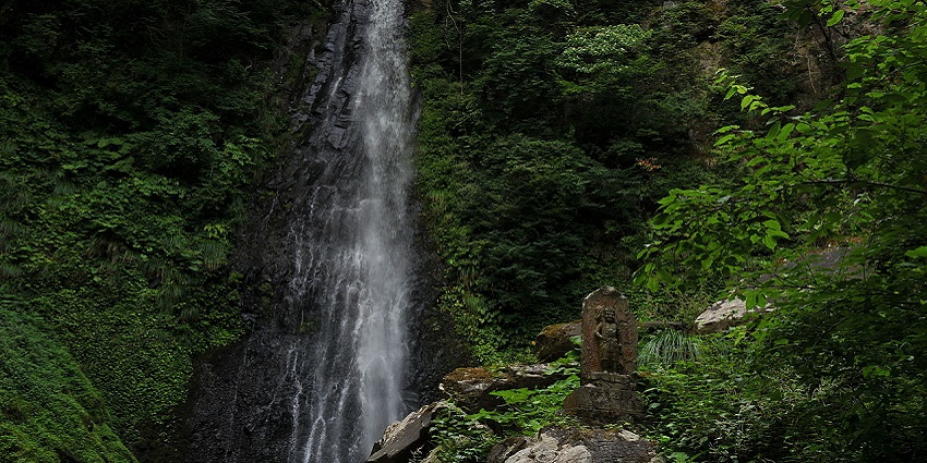 Amedaki Falls cascade from a stone with a small engraved statue in serene surroundings