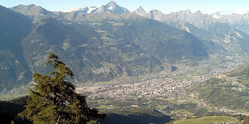 Aosta Valley with a lake and distant town buildings surrounded by big green mountains