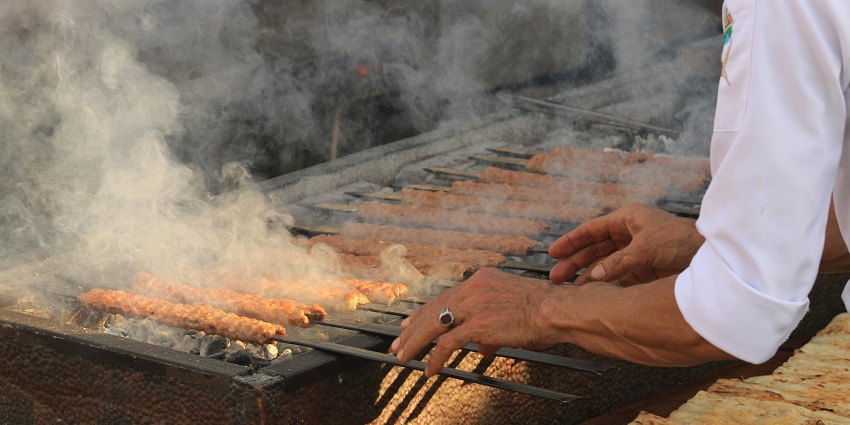 Two traditional metal grills with large-cut meat arranged vertically above an open fire.