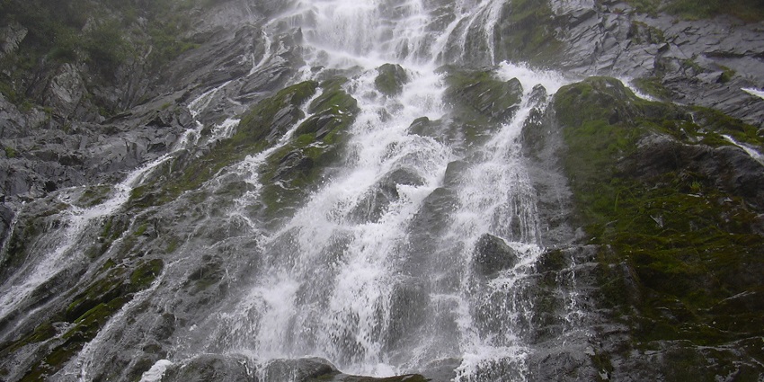 The Bâlea Waterfall descends from the mountain slope as mist rises from the air.