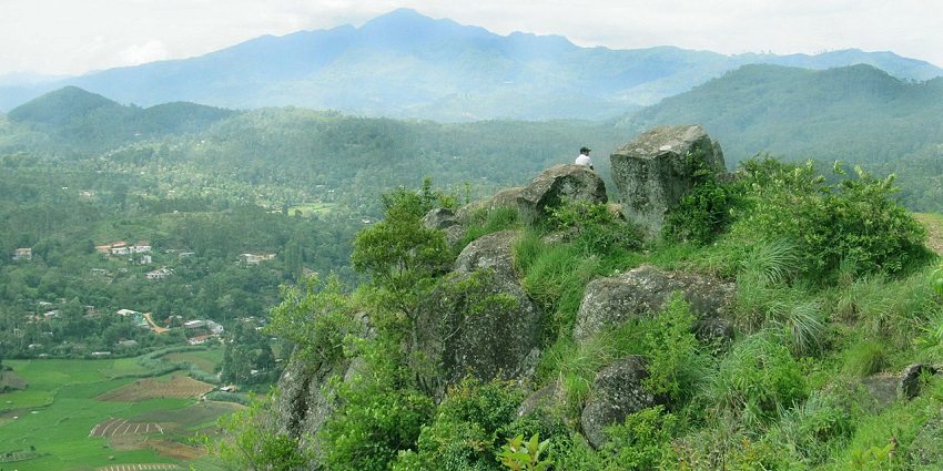 A man enjoys the view of Bandarawela in Sri Lanka from a high and rocky viewpoint.