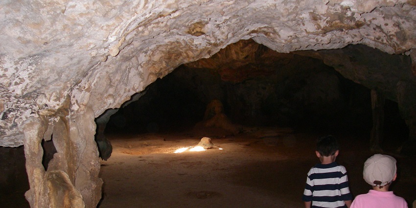 A small, rugged entrance to one of the Aruba caves surrounded by dry terrain.