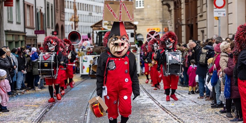 Performers in colorful costumes and masks parade at a lively Swiss Basel carnival.