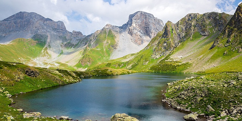 All bright hues in one frame depict a stunning blue lake amidst lush green hills and rocks.