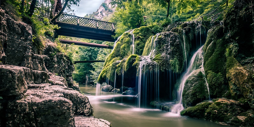 Water is cascading over mossy rocks at Bigăr Waterfall, creating a magical forest scene.