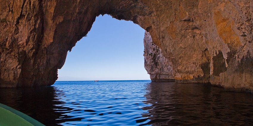 An image of a boat entering the Blue Grotto cave with glowing blue waters at Malta caves.