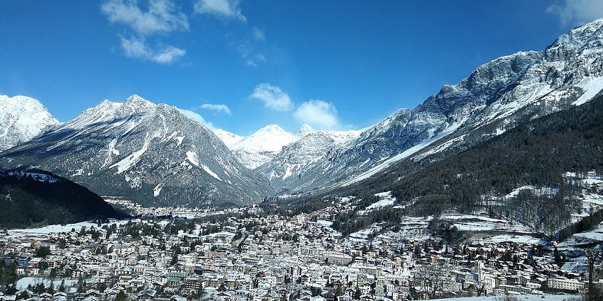 Bormio town with distant buildings, houses fully covered in white snow and mountains