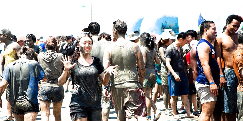 A person rubbing mud on another person's face and others standing behind covered in mud