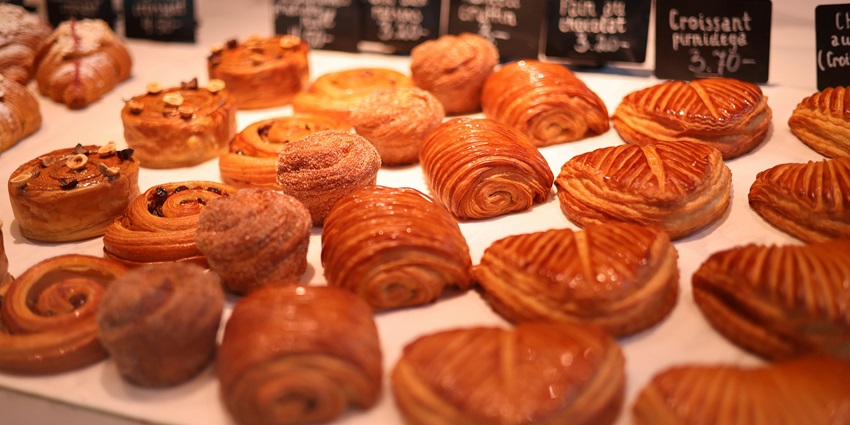 A rustic wooden table inside a cosy café displays freshly baked croissants and pastries.