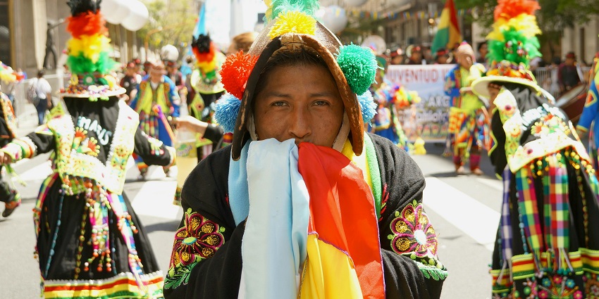 A man in a colourful costume looks into the camera with parade members in the background.