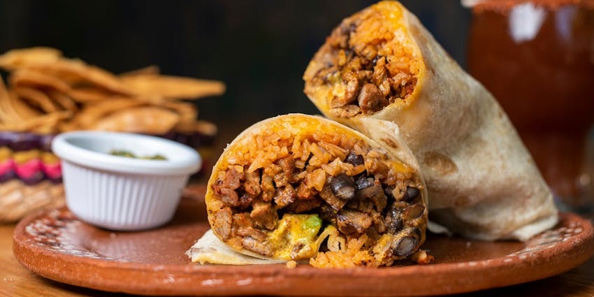 A loaded burrito cut in half, filled with rice, beans, cheese, and grilled meat.