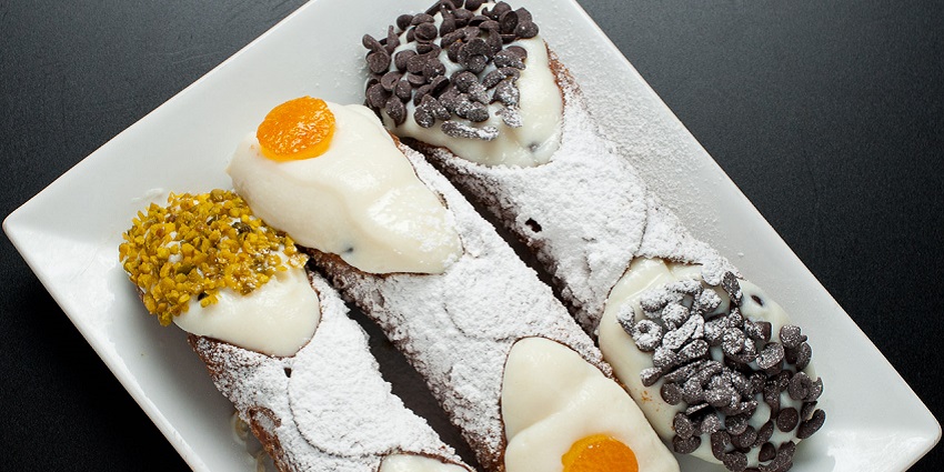 Crispy Sicilian cannoli shell filled with creamy ricotta and chocolate chips, a popular street food in London.