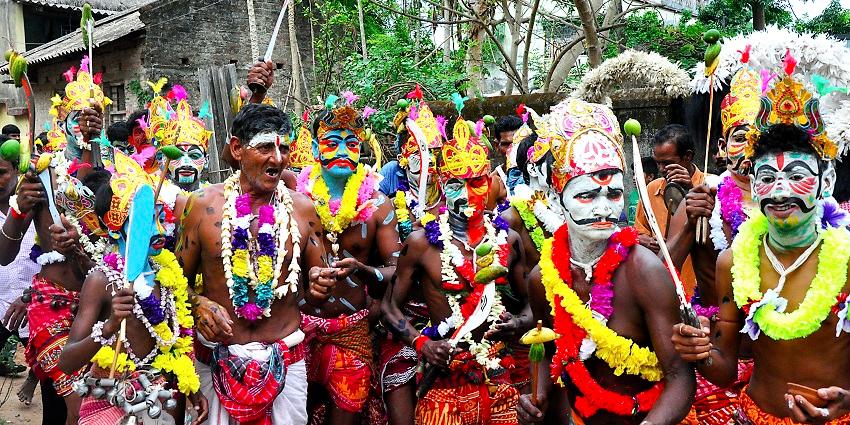 A group of men with painted faces all decked up weirdly for a street show for their fellow spectators.