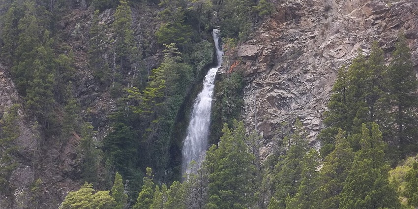 A waterfall cascades from a cliff at rugged Cascada de la Virgen in lush greenery.