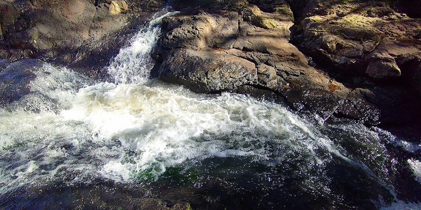 Salto Kinas waterfall pours down rugged rock formations into a still, rocky basin below.