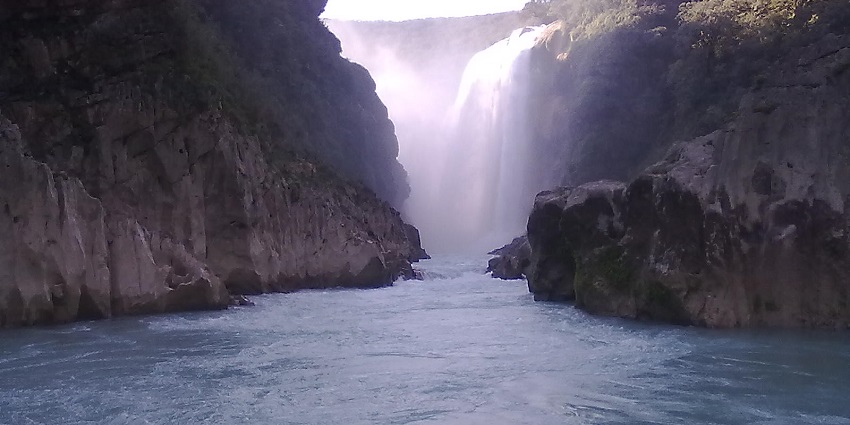 Cascada Tamúl waterfall rushes over wide rocks into a blue river surrounded by jungle.