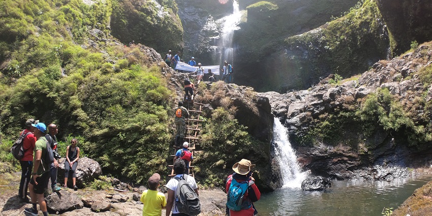 Cascade 500 Pieds with tourists climbing a ladder, surrounded by lush greenery and rocks