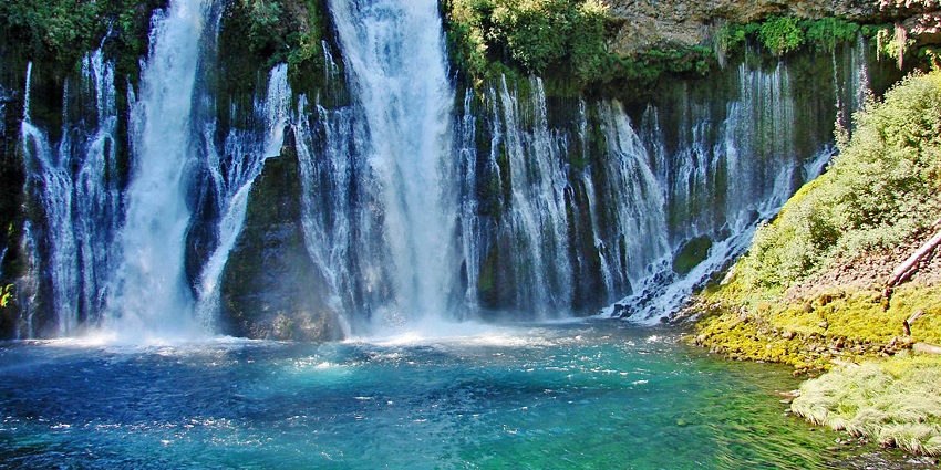 Waterfall flowing into a turquoise pool from a rocky cliff covered in greenery in a park