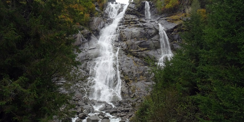 Waterfall cascading through a rocky cliff and stones surrounded by dense green vegetation