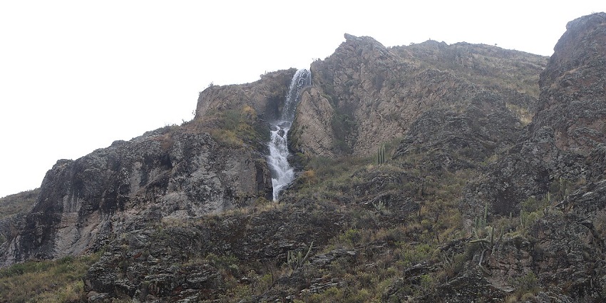 Waterfall with water flowing on the rocky surface and dried-out brown grass on the hill