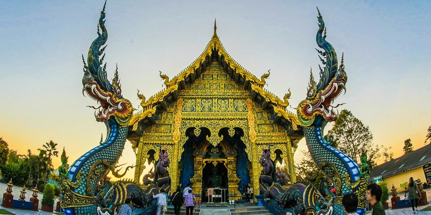 Colorful dragon statue with green and gold scales at sunset, overlooking hills and moonlit sky in Chiang Rai.