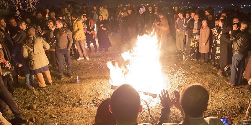 People standing in a circle with a small fire in the middle and some warming their hands