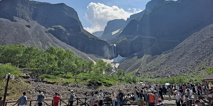 The silver water of Changbai Falls is surrounded by mist cascading through rocky mountains.