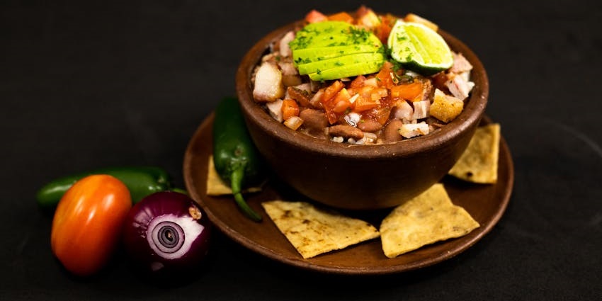 An image showing dipping sauce with sliced vegetables and nachos, similar to Chifrijo.