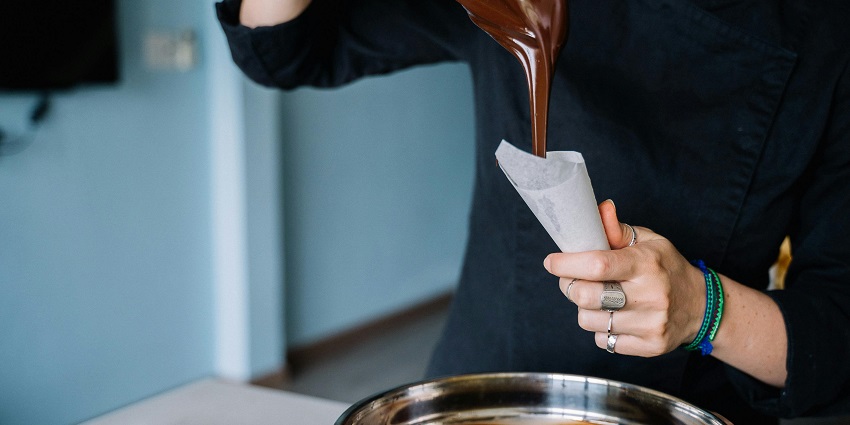 Image of a woman pouring melted chocolate into a piping bag at a Brussels workshop.
