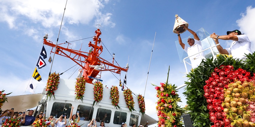 A man carrying an idol and another clapping while standing in a boat decorated with flowers