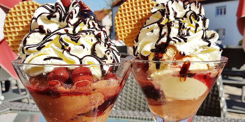 Scoops of colourful ice cream served in a bowl, with waffle cone pieces on a wooden table.