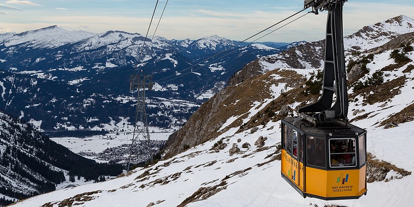 People take the gondola ride from one mountain peak to the other covered with snow on a cloudy day.