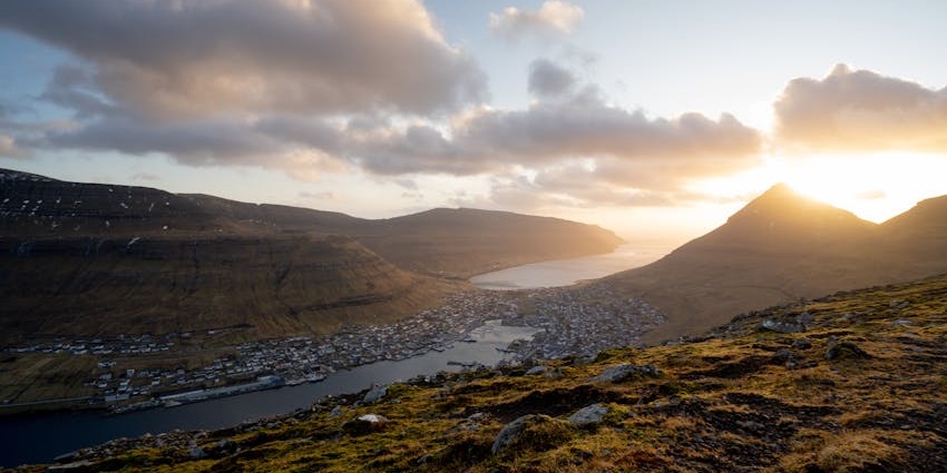 Sunset over a coastal side surrounded by rugged mountains and a winding body of water.