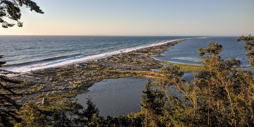 A narrow sand spit stretching into the sea with a scenic lighthouse and a coastal hiking trail.