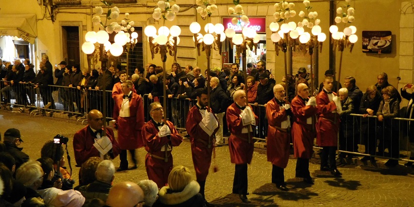 Hooded participants walk in rows, holding religious statues during an Easter procession