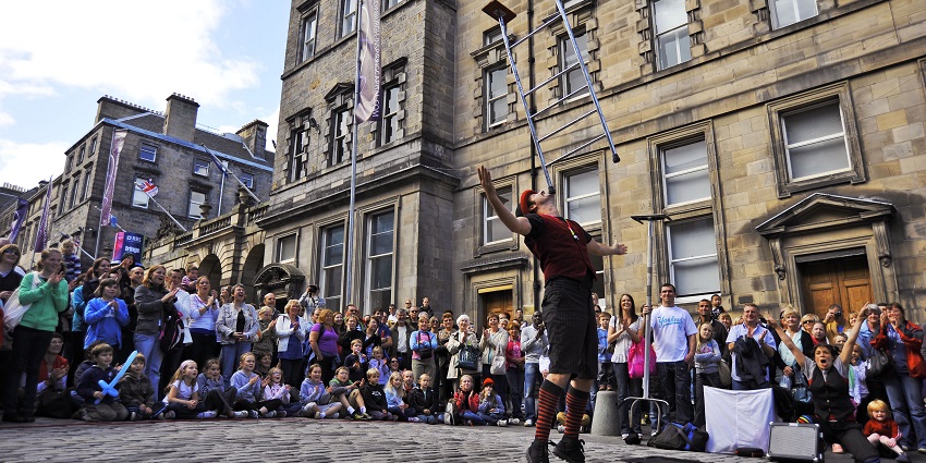 A street performer balances a small ladder on his jaw while the audience cheers